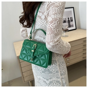 Detail of green quilted crossbody bag with golden metal lock worn by a model in interior