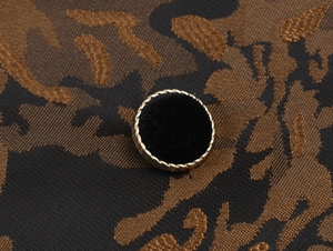Détail d'un bouton vintage en velours noir avec bordure dorée sur une robe en jacquard