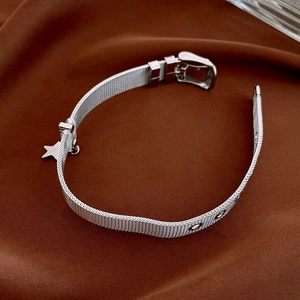 Close-up of silver Milanese mesh bracelet with star pendant on brown textured fabric