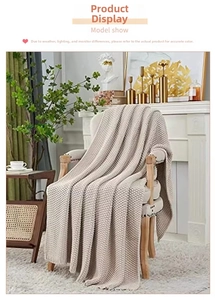Detail of a cozy beige chunky knit blanket with tassels draped on a wooden chair
