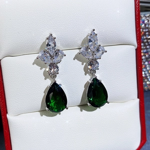 Macro view of clover-shaped zircon earrings with pear-cut green emerald-like gemstone drop