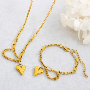Detail of gold stainless steel heart pendant necklace and bracelet set on stone background