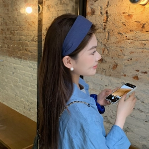 Navy blue fabric headband with wide plaid texture shown on a model against a brick wall