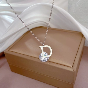 Macro detail of silver D-letter necklace with a round cubic zirconia on white silk background