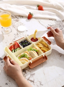Detail view of a beige multi-compartment bento box with sandwich, fries, and fresh fruit