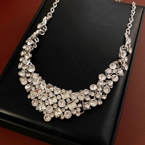 Macro shot of silver crystal necklace with geometric rhombus pendant on black tray