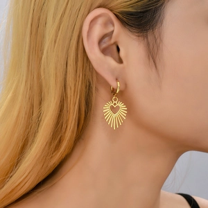 Close-up of a model wearing a gold heart-shaped earring with sunburst diamond design