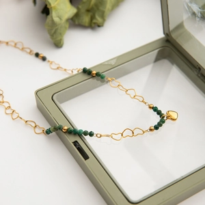 Close-up of golden necklace with green beads and heart pendant on a glass box