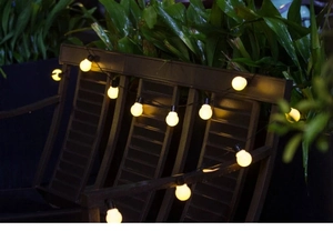 Detail of warm white G50 solar LED string lights hanging on a wooden garden chair