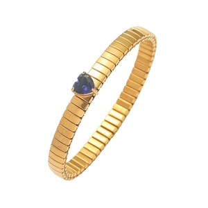 Detail of a golden elastic bracelet featuring a heart-shaped deep blue sapphire stone