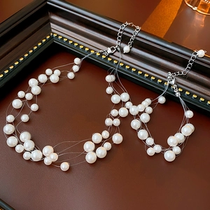 Detail of layered white pearl necklace and bracelet set on dark leather surface