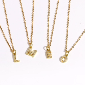 Close-up of four gold letter necklaces L, M, E, O with sparkling zircon inlay details