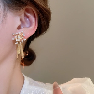 Close-up of golden starburst tassel earrings with pearls and rhinestones on model
