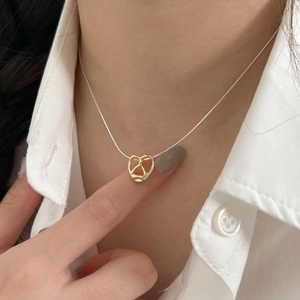 Minimalist gold knotted heart pendant on thin silver chain worn with a white shirt