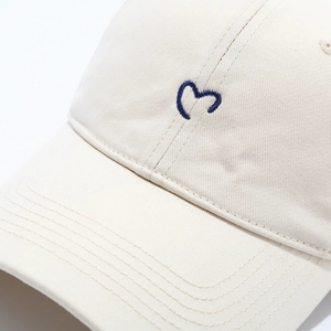 Detailed close-up of blue heart embroidery on cream cotton baseball cap with fine stitching