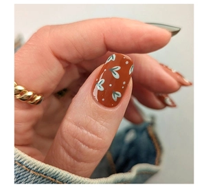 Close-up of retro red-brown press-on nails with green heart patterns and a gold rope ring