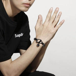 Détail d'un bracelet en cuir tressé noir avec fermoir mousqueton en métal au poignet