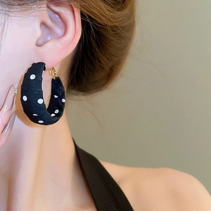 Close-up of stylish black polka dot fabric wrapped hoop earring on a model ear