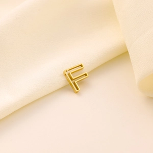 Détail d'un pendentif lettre F dorée ajourée avec finition mate sur tissu satiné