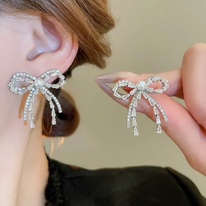 Close-up of bow earrings with tassels, white pearls and sparkling zircon inlays