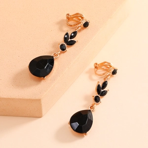 Detail of gold clip-on earrings with black teardrop gemstones on a textured display