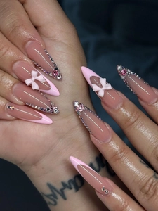 Macro shot of long pointed press-on nails with pink French tips and 3D bow accents