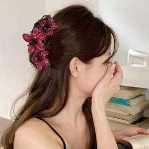 Macro detail of large deep purple floral hair claw clip worn on model's ponytail