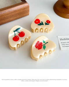 Three small cream acetate hair claws with cherry and floral prints on a desk