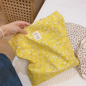 Detail of yellow floral cotton tote bag featuring white woven label in a home setting