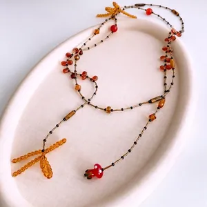 Handmade beaded necklace with mushroom pendant and amber bow on a cream tray