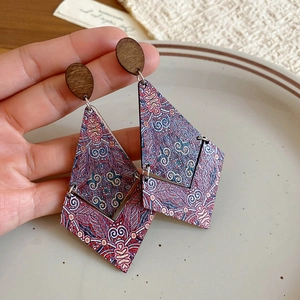 Close-up of geometric diamond-shaped wooden earrings with mandala patterns and retro motifs