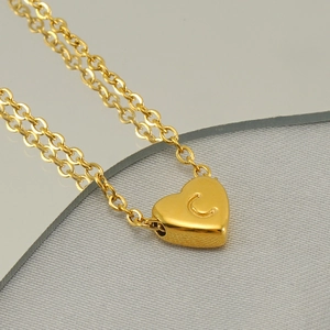 Macro shot of gold heart pendant with letter C engraving on a polished O-chain necklace