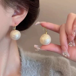 Détail d'une grande boucle d'oreille en perle blanche avec anneau doré porté par un modèle