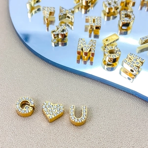 Close-up of gold-plated G and heart beads with white zircons for DIY jewelry making