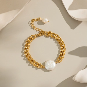 Close-up of gold chain bracelet with large baroque pearl on a minimalist stone base