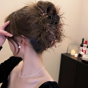 Detailed view of hair claw clip with dark feathers and pearls on elegant hair bun