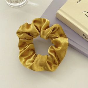 Detailed view of yellow satin scrunchie with silky texture on light tabletop