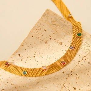 Golden mesh necklace with colorful gemstones displayed on a beige textured stone
