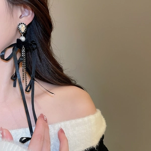 Détail de boucles d'oreilles longs rubans noirs avec franges métalliques et strass brillants