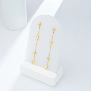 Detailed view of elegant gold star tassel earrings on a white geometric display stand