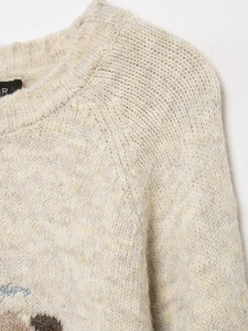 Detail of cream wool blend knit sweater featuring ribbed crew neck and blue embroidery