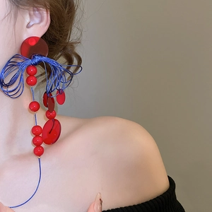 Close-up of artistic red resin and blue silk tassel knot earrings on a female model