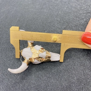 Detail view of measuring a gold-plated acrylic bull skull pendant with a brass caliper