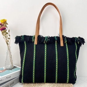 Black woven beach tote bag with green stripes, tassels, and brown leather handles