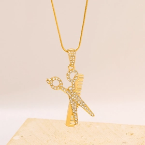 Gold pendant necklace with crystal-encrusted scissors and comb on a stone base