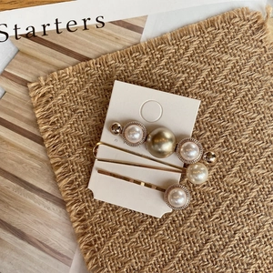 Close-up of vintage pearl chain hair clips with gold metal finish on a textured background
