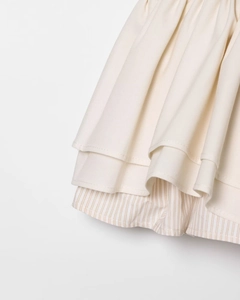Detailed close-up of ivory ruched fabric layered over beige pinstripe mini dress