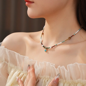 Detail of bohemian pearl and turquoise necklace with gold accents worn by a model