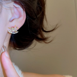 Detail of gold rocking horse earring with crystals and red accents on a model ear