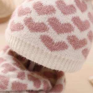 Detail eines warmweißen Baby-Stricksets mit Mütze und Schal und rosa Herz-Mustern